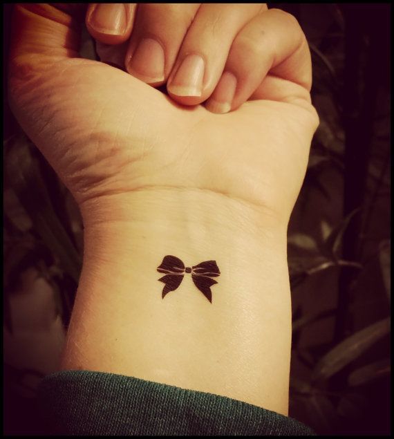 Tiny black bow tattoo on girl’s wrist